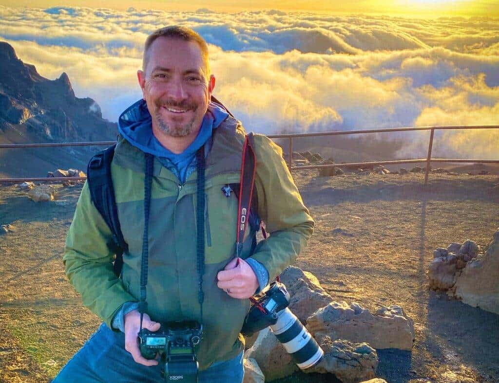 Photographer smiling at mountain sunset with camera gear